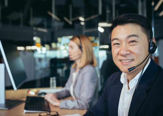 closeup-portrait-asian-man-business-attire-call-center-employee-looks-camera-smiles-businessman-uses-computer-video-call-headset 1